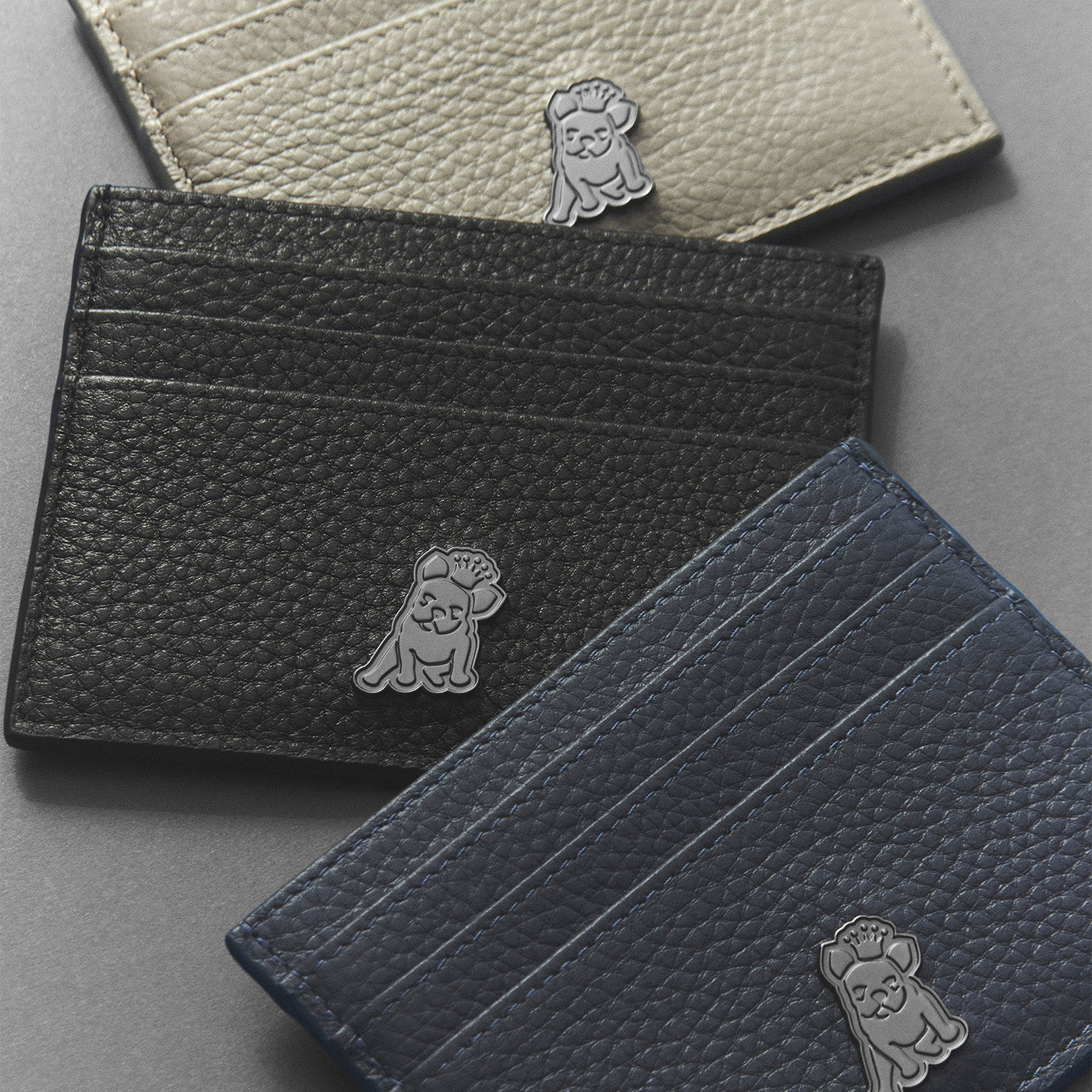 Three leather card holders in black, gray, and blue with a dog emblem on a gray background.