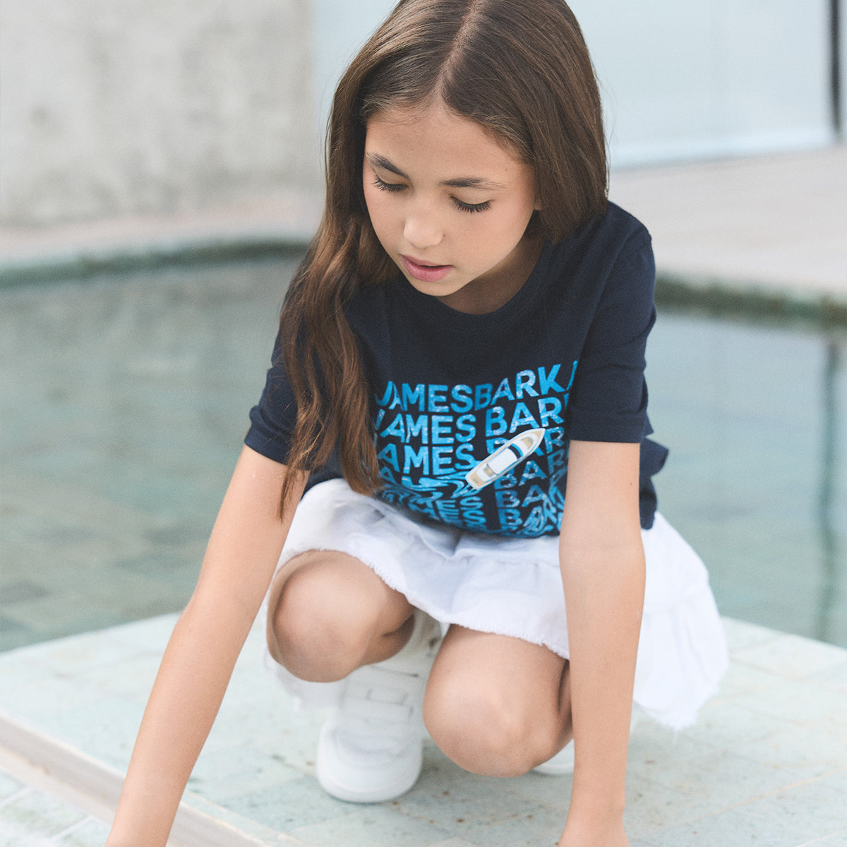 Young girl playing outdoors wearing a navy blue James Bark graphic t-shirt with a boat design and white skirt