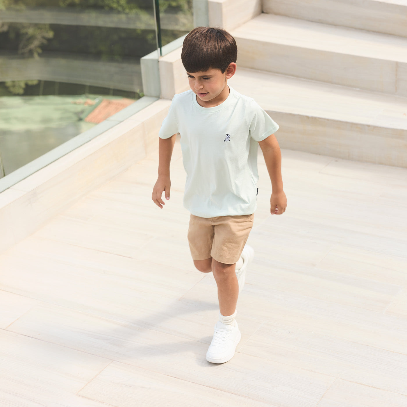 Young boy wearing a light green James Bark crew neck t-shirt and khaki shorts running down outdoor stairs.