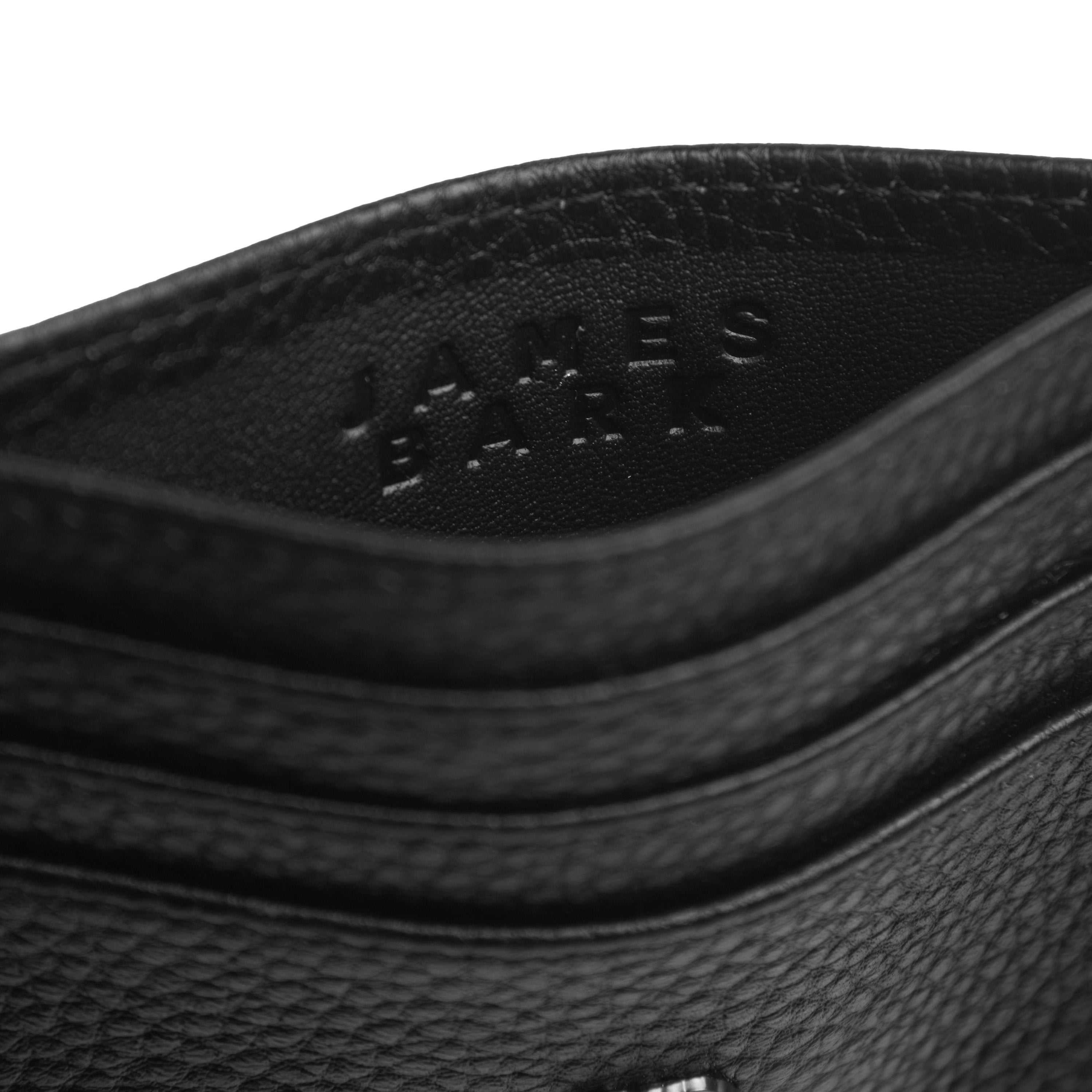 Close-up view of a black textured leather cardholder with the embossed text 'JAMES BARK' on the inside. The stitching and grain detail of the leather are prominently visible.