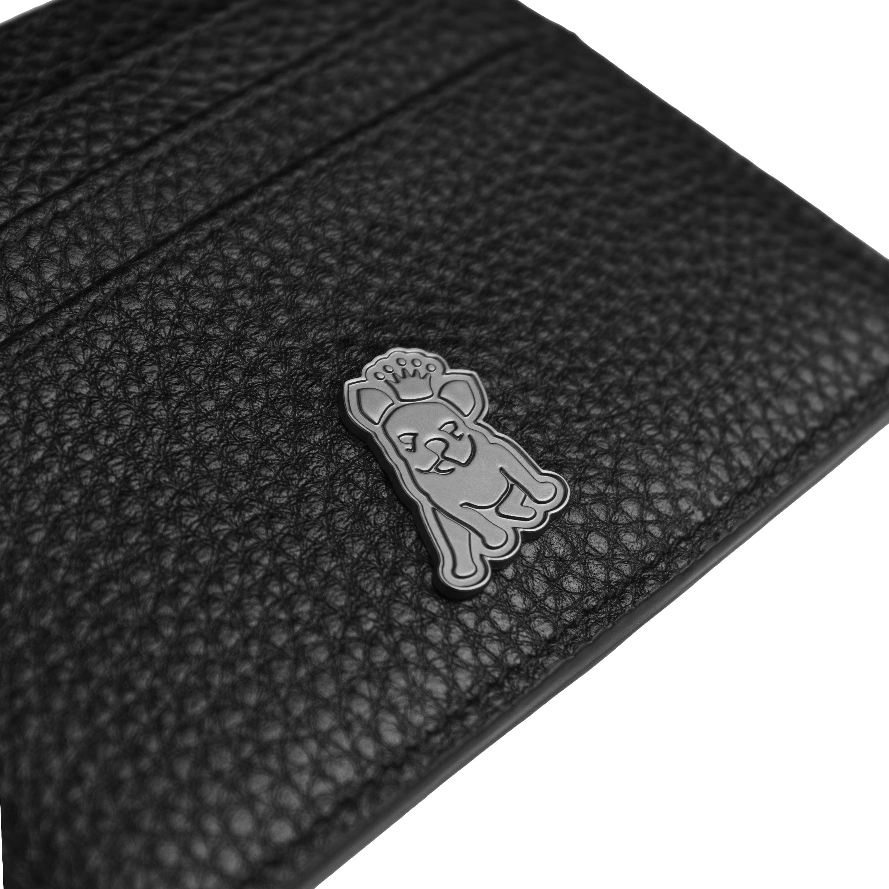 Close-up view of a black textured leather cardholder featuring a small metallic emblem of a dog with a crown, adding a unique branding element to the accessory.