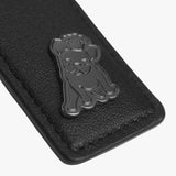 A close-up view of a black leather tag featuring a metallic emblem of a dog wearing a crown, with detailed stitching along the edges.