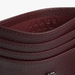 Close-up view of a deep red textured leather cardholder featuring a small metallic emblem of a dog with a crown, adding a unique branding element to the accessory.