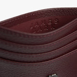 Close-up view of a deep red textured leather cardholder featuring a small metallic emblem of a dog with a crown, adding a unique branding element to the accessory.