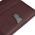 Close-up view of a deep red textured leather cardholder featuring a small metallic emblem of a dog with a crown, adding a unique branding element to the accessory.