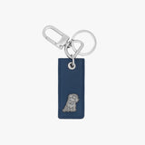 Minimalist keychain featuring a rectangular navy blue leather tag with a small embossed dog logo at the bottom. Attached to the tag are a silver keyring and a clasp hook for added functionality.