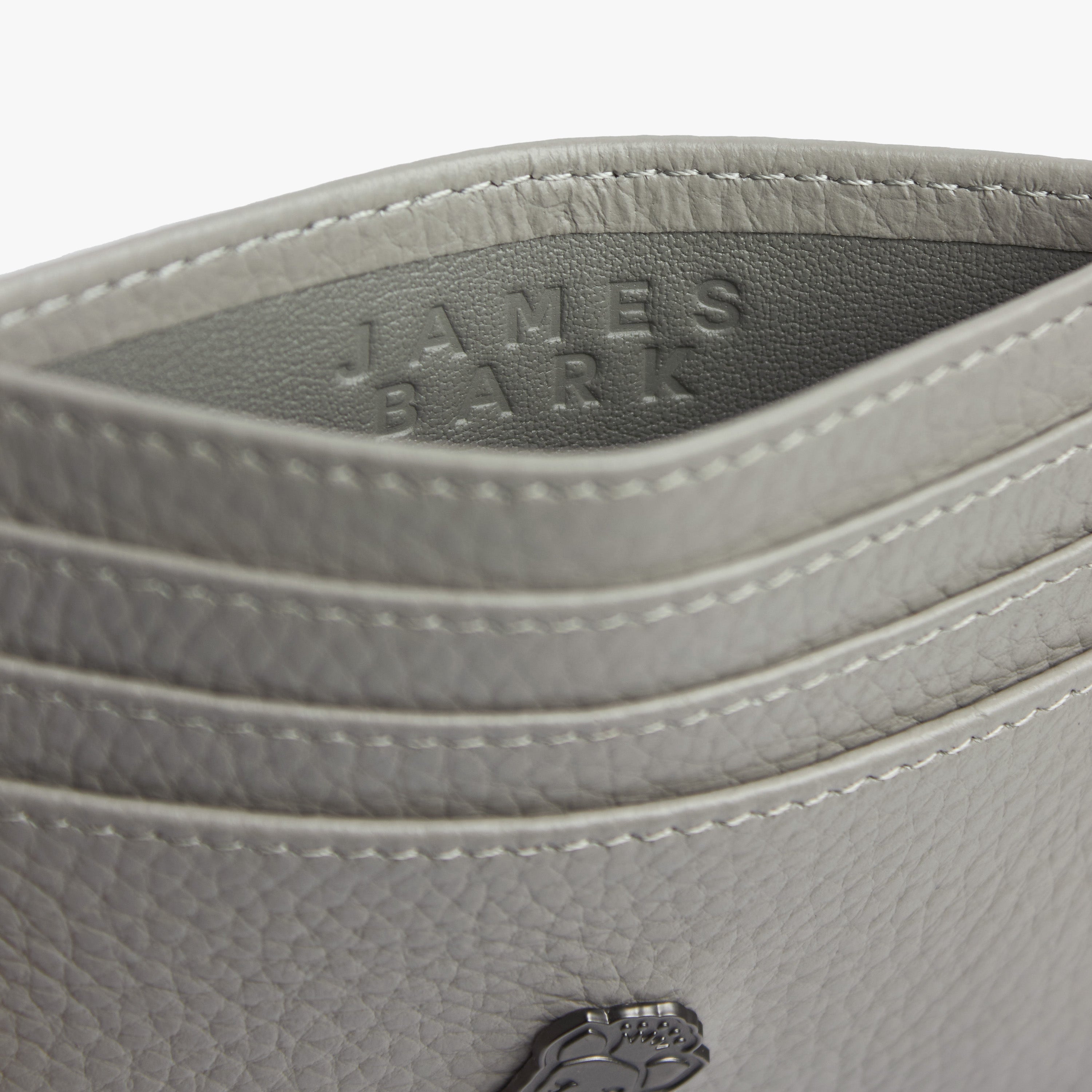 Close-up view of a gray textured leather cardholder with the embossed text 'JAMES BARK' on the inside. The stitching and grain detail of the leather are prominently visible.