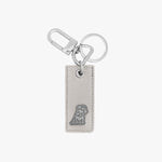 Chic keychain featuring a rectangular light gray leather tag with a silver embossed dog logo at the bottom. The tag is connected to a polished silver keyring and a clasp hook, offering a stylish and functional design.