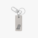 Chic keychain featuring a rectangular light gray leather tag with a silver embossed dog logo at the bottom. The tag is connected to a polished silver keyring and a clasp hook, offering a stylish and functional design.