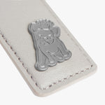 A close-up view of a white leather tag showcasing a metallic emblem of a dog wearing a crown, with subtle stitching details.