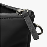 A close-up of the zipper and hardware details of a black tote bag. The zipper pull is made of black material with the brand name "JAMES BARK" embossed on it. The zipper itself is sturdy, with a smooth metal finish. A metal ring is attached near the zipper, suggesting an option for additional attachments or a shoulder strap. The stitching and matte finish of the bag highlight its sleek and durable construction.