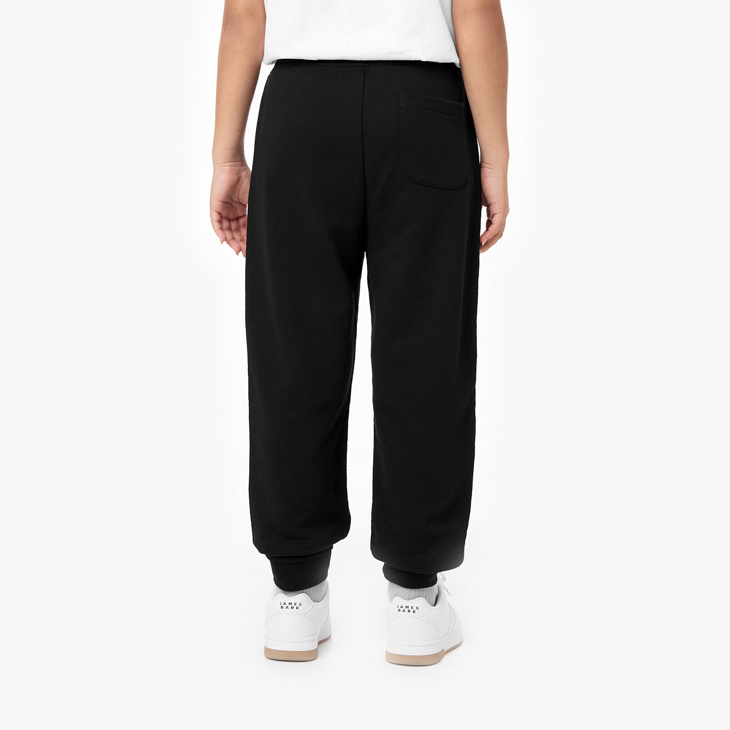 Back view of black jogger pants with elastic cuffs, styled with white sneakers