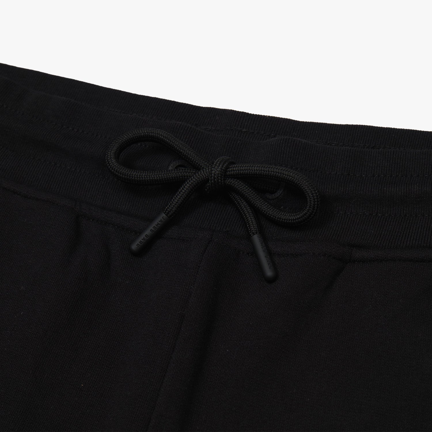 Close-up of the waistband and drawstring of black jogger pants, showing a neatly tied bow with branded aglets on the drawstrings. The texture of the fabric and ribbed waistband is visible