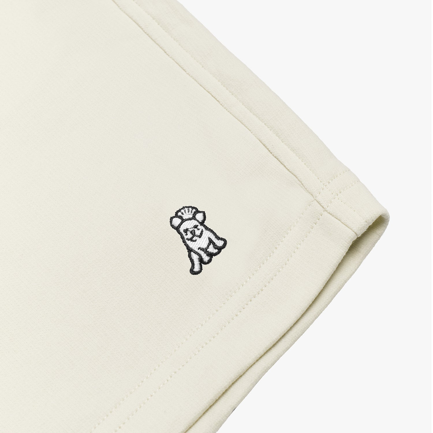 Close-up of the embroidered dog logo on cream-colored shorts, highlighting the detailed stitching and fabric texture