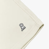 Close-up of the embroidered dog logo on cream-colored shorts, highlighting the detailed stitching and fabric texture