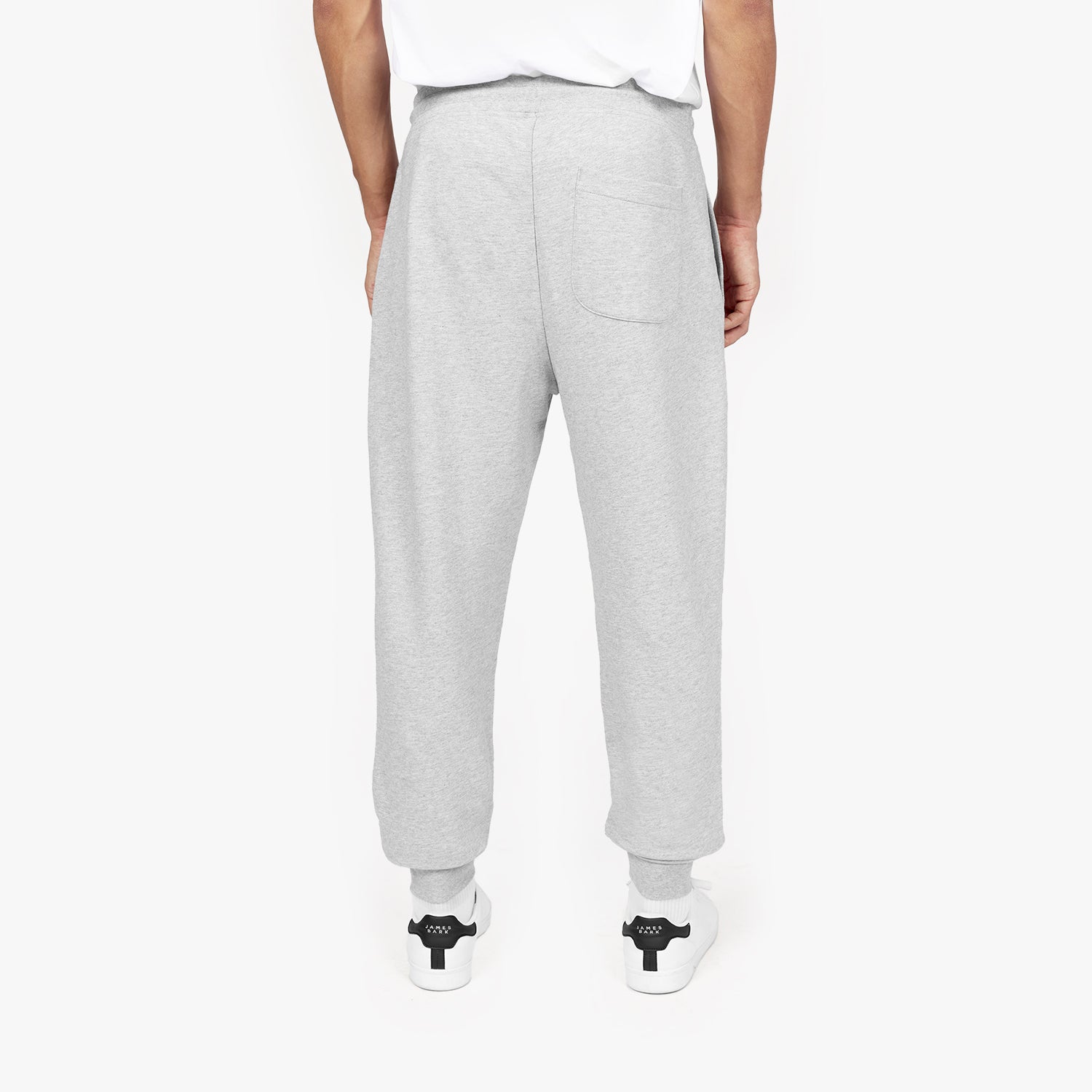 Back view of a person wearing light gray jogger-style sweatpants with a single back pocket, paired with white sneakers featuring black accents. The person is also wearing a white T-shirt, and the background is plain white." Let me know if any edits are needed