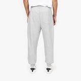 Back view of a person wearing light gray jogger-style sweatpants with a single back pocket, paired with white sneakers featuring black accents. The person is also wearing a white T-shirt, and the background is plain white." Let me know if any edits are needed