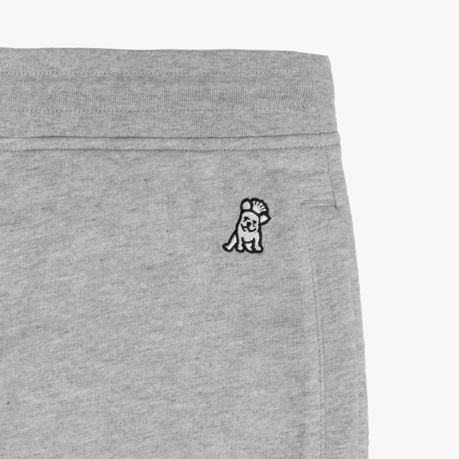 Close-up detail of light gray jogger-style sweatpants showing an embroidered black and white dog logo near the waistband. The sweatpants feature a clean and minimal design, displayed against a plain white background." Let me know if you'd like any modifications