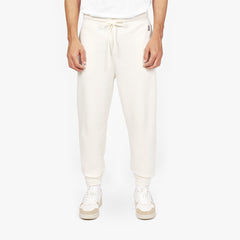 Front view of a person wearing off-white jogger-style sweatpants with a drawstring waist and cuffed ankles, paired with white sneakers featuring beige accents. The person is also wearing a white T-shirt, and the background is plain white." Let me know if you'd like any changes