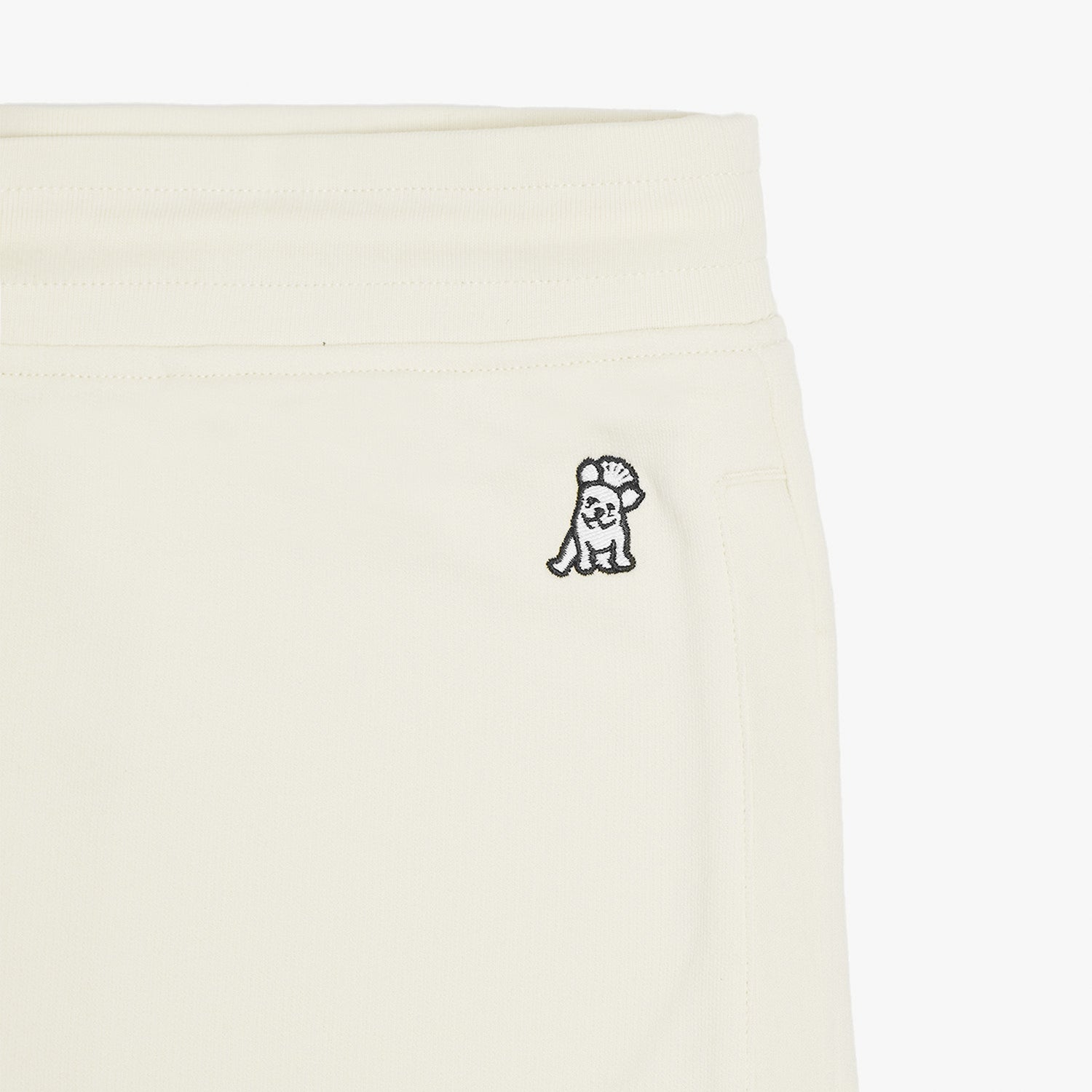 Close-up of the embroidered dog logo on the cream-colored jogger pants, near the waistband, showcasing detailed stitching