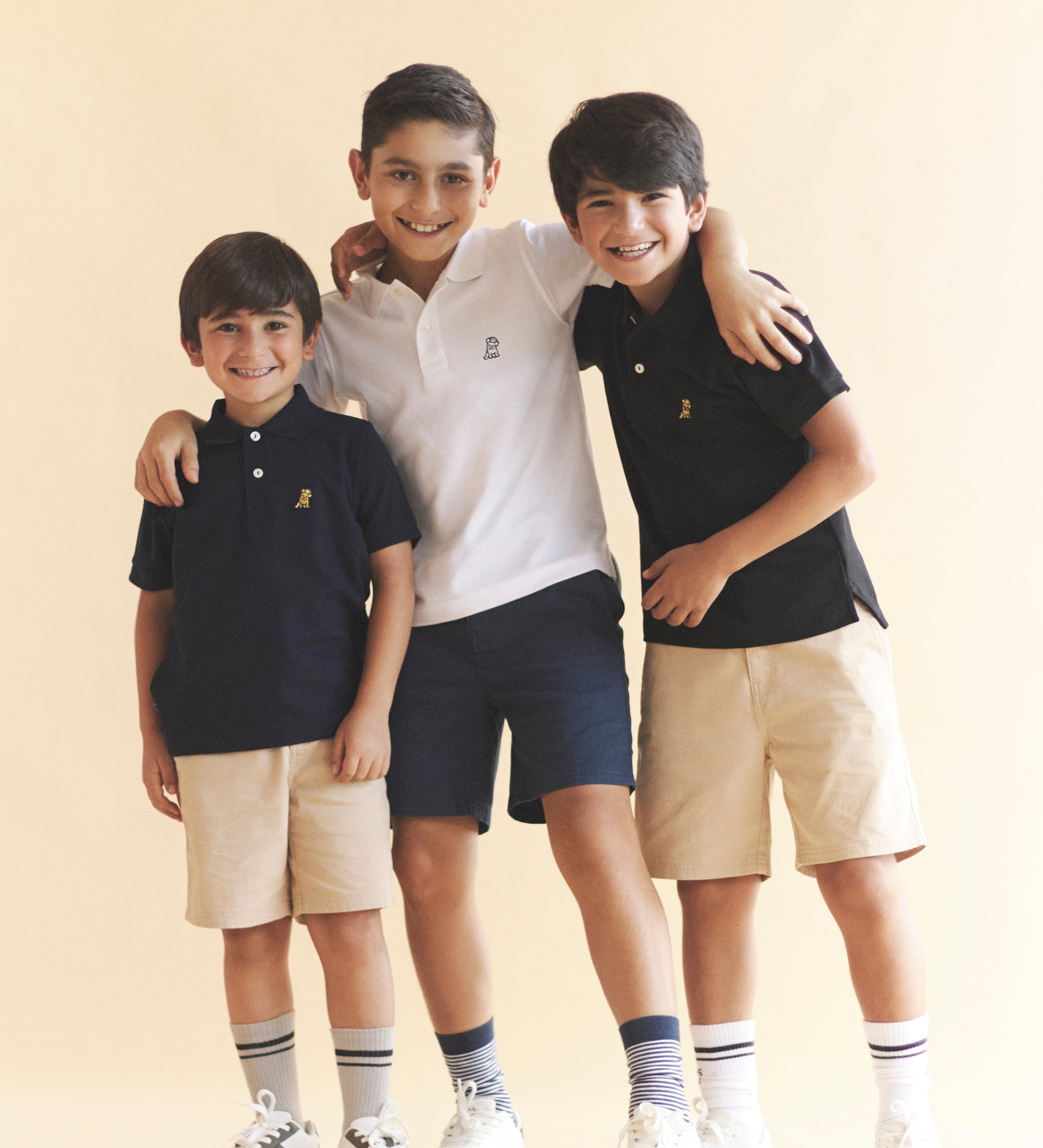 Three children in matching outfits standing together against a beige background