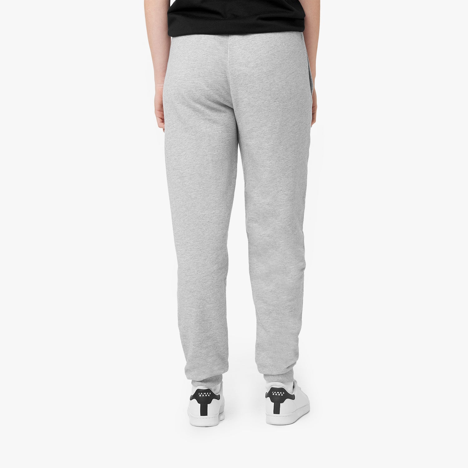 This image shows the back view of the light grey sweatpants from the previous image. The pants have a simple design with a clean, tailored look, offering a comfortable, fitted feel. The sneakers in this image feature a distinctive black and white design, complementing the overall sporty aesthetic.