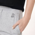 This close-up image shows the small embroidered design of a dog with a helmet, located near the pocket of the grey sweatpants. It’s a cute and distinctive detail, adding some personality to the otherwise simple and casual look.