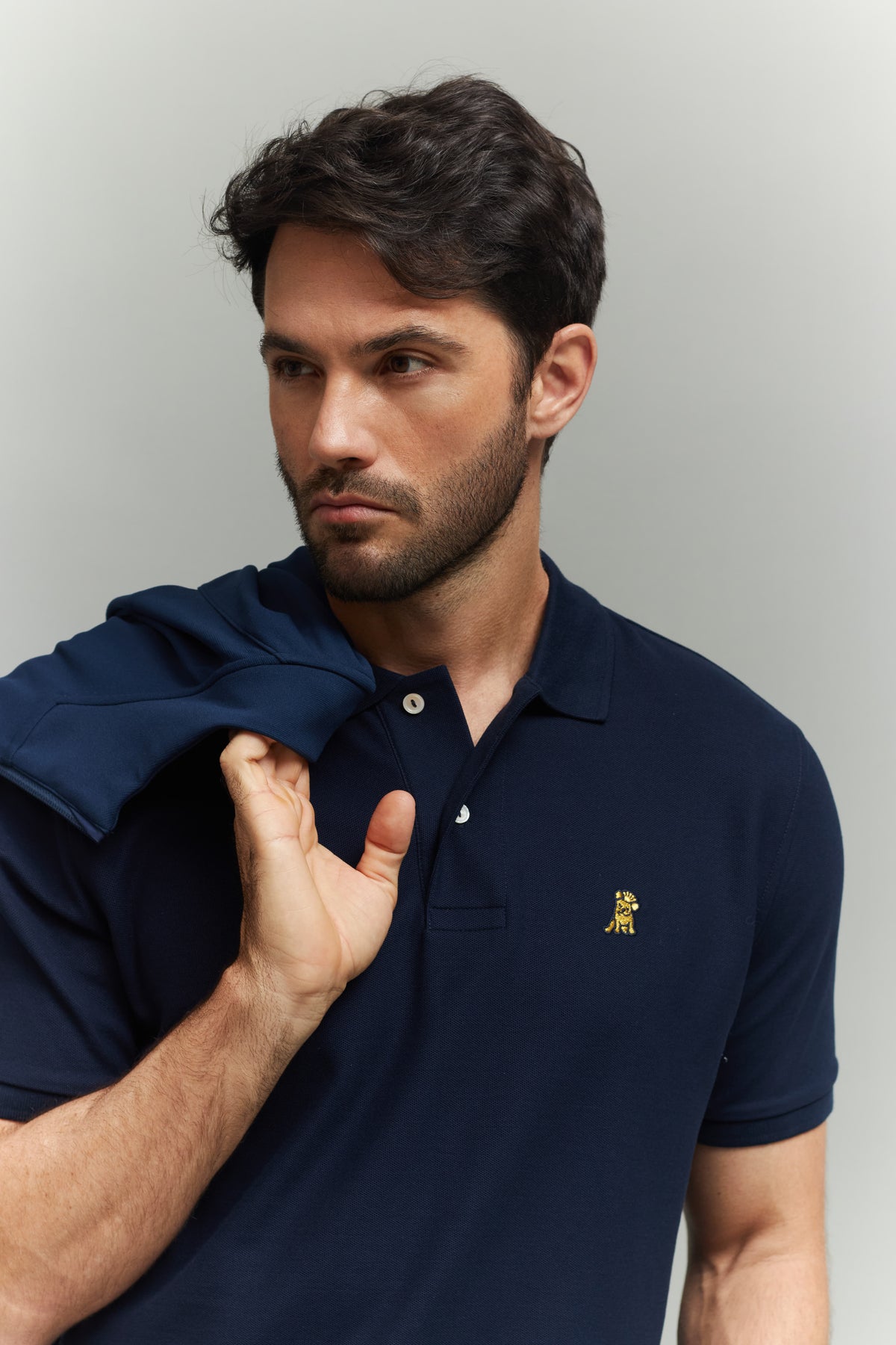 Man wearing a navy blue polo shirt with a gold embroidered dog logo on the left side chest