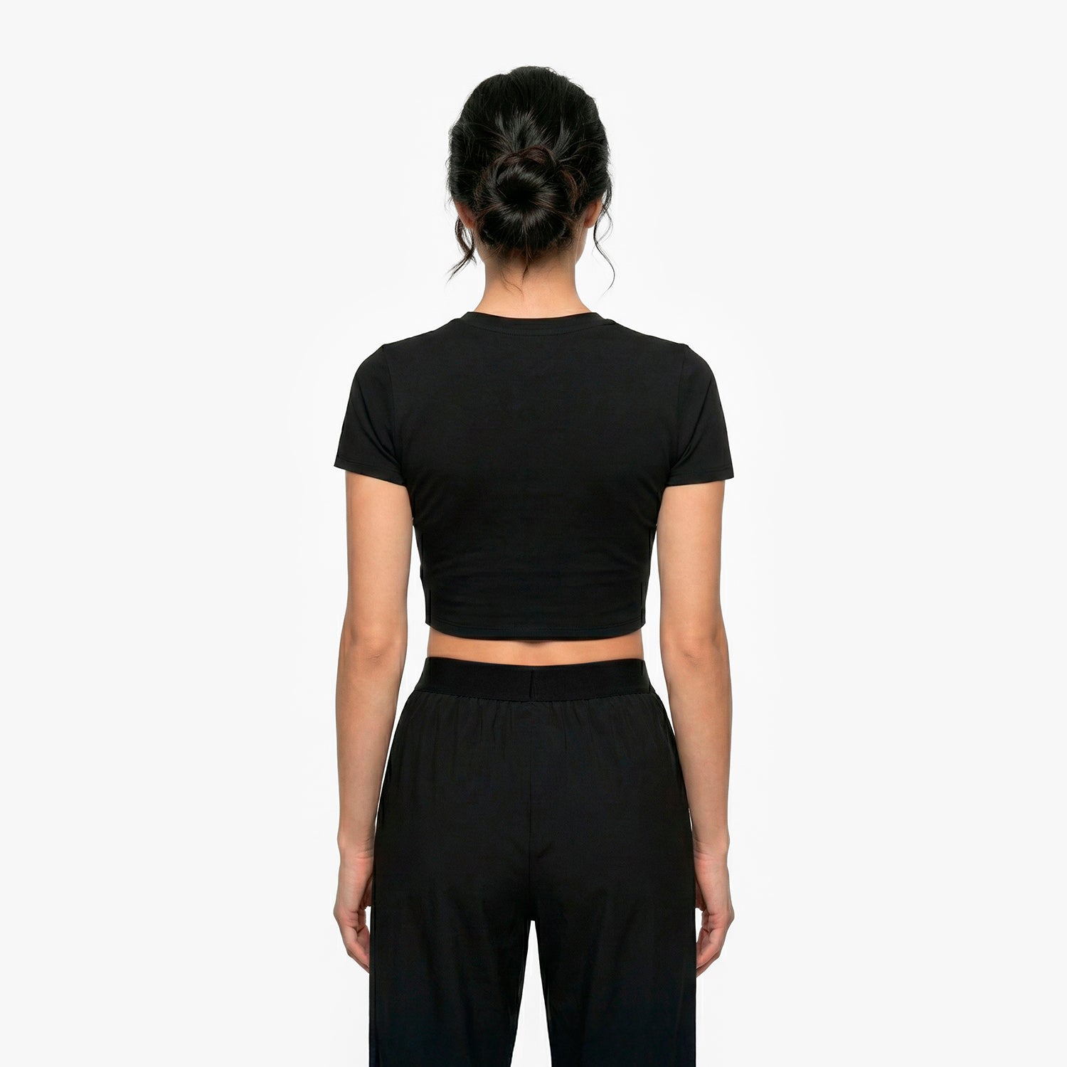 Person wearing a black crop top and black pants on a white background