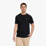 A man wearing a black T-shirt with a small white embroidered logo on the left chest, paired with khaki pants
