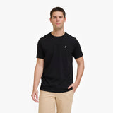 A man wearing a black T-shirt with a small white embroidered logo on the left chest, paired with khaki pants