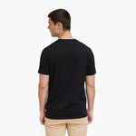 A man viewed from the back, wearing a plain black short-sleeve crewneck t-shirt and beige pants