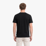 Man wearing a black t-shirt and light-colored pants on a white background