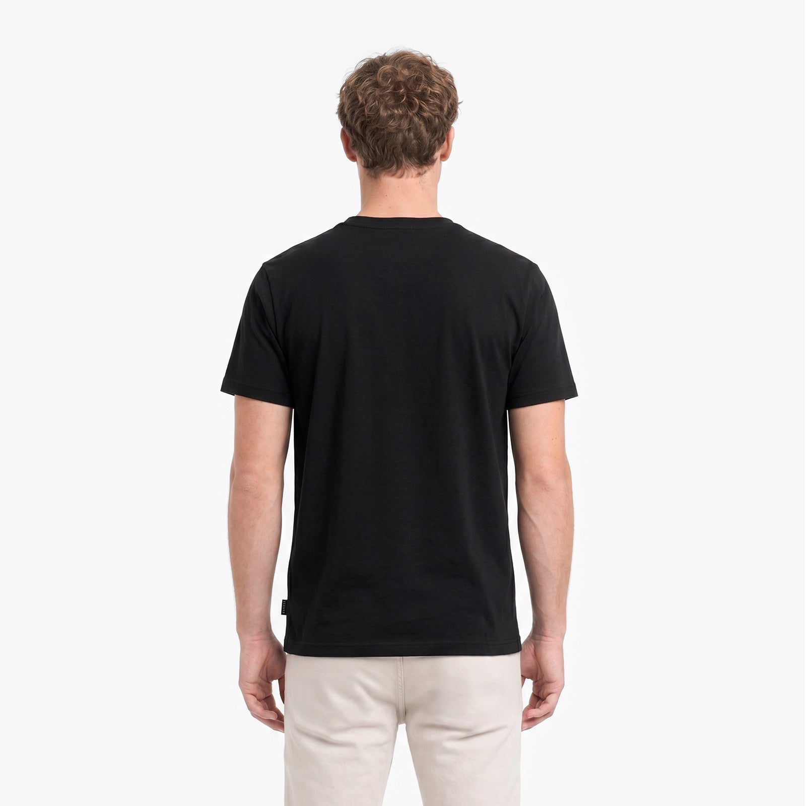 Man wearing a black t-shirt and light-colored pants on a white background
