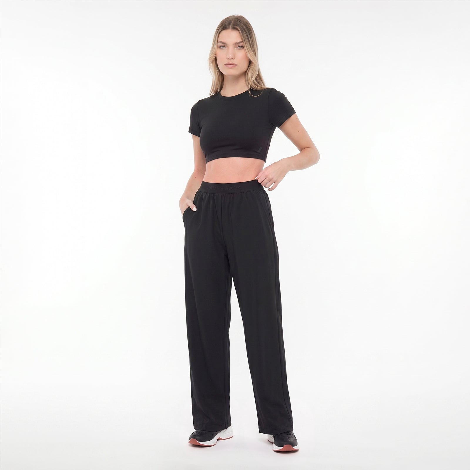 Woman wearing a black crop top and black pants on a white background