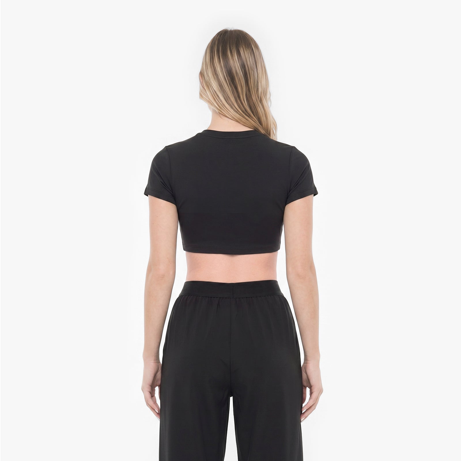 Person wearing a black crop top and black pants on a white background