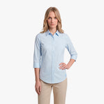 Woman wearing a light blue button-up shirt and beige pants on a white background