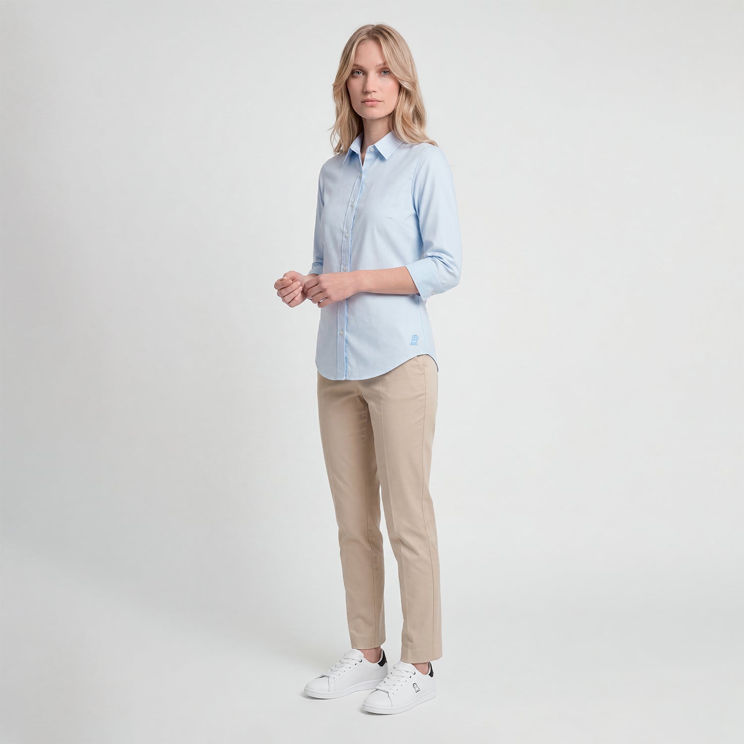 Woman wearing a light blue shirt and beige pants on a white background
