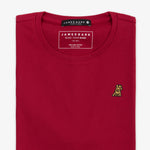  Close-up of the neckline of a red T-shirt, showing the small golden embroidered logo on the chest and internal tag.