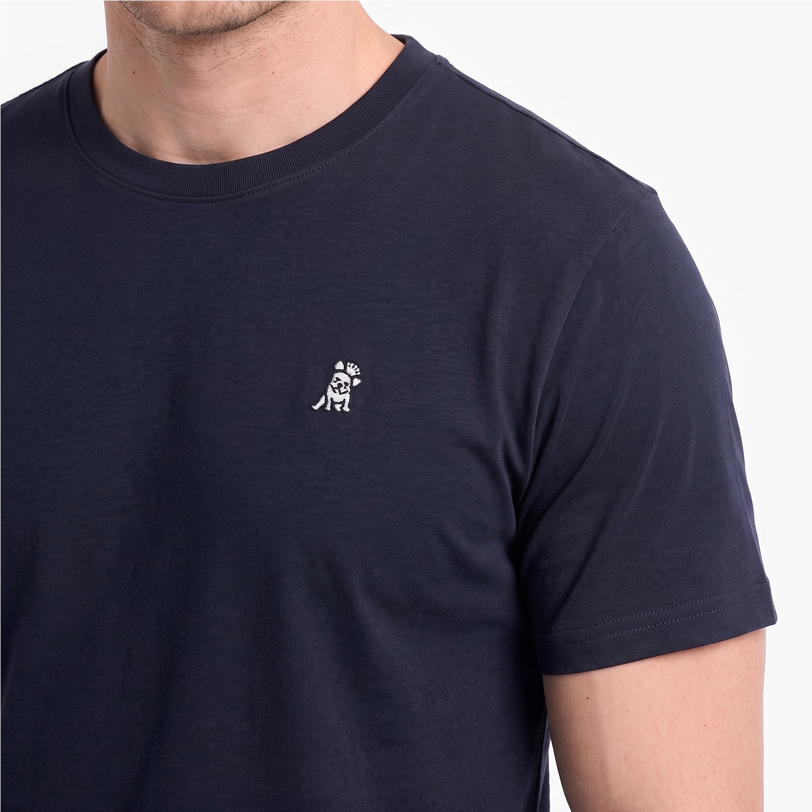 A close-up of a man wearing a navy blue crew-neck t-shirt with a small white embroidered dog logo