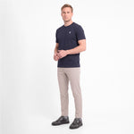 A man wearing a short-sleeve crewneck t-shirt in navy blue with a small white logo on the left chest, paired with beige trousers