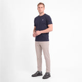 A man wearing a short-sleeve crewneck t-shirt in navy blue with a small white logo on the left chest, paired with beige trousers