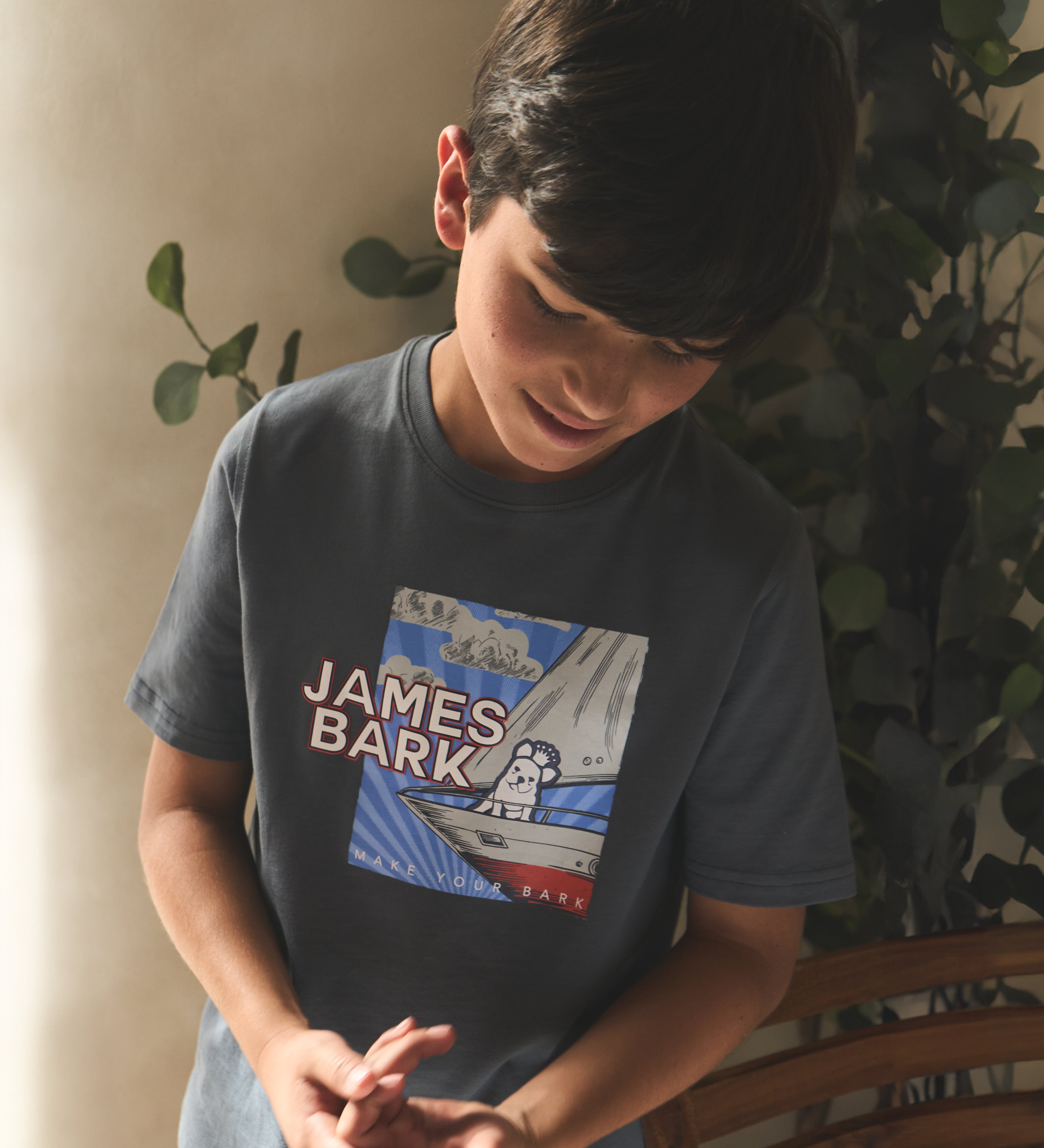 Young boy wearing a t-shirt with 'James Bark' design, standing indoors.