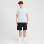 Man wearing a light blue t-shirt and black shorts on a white background