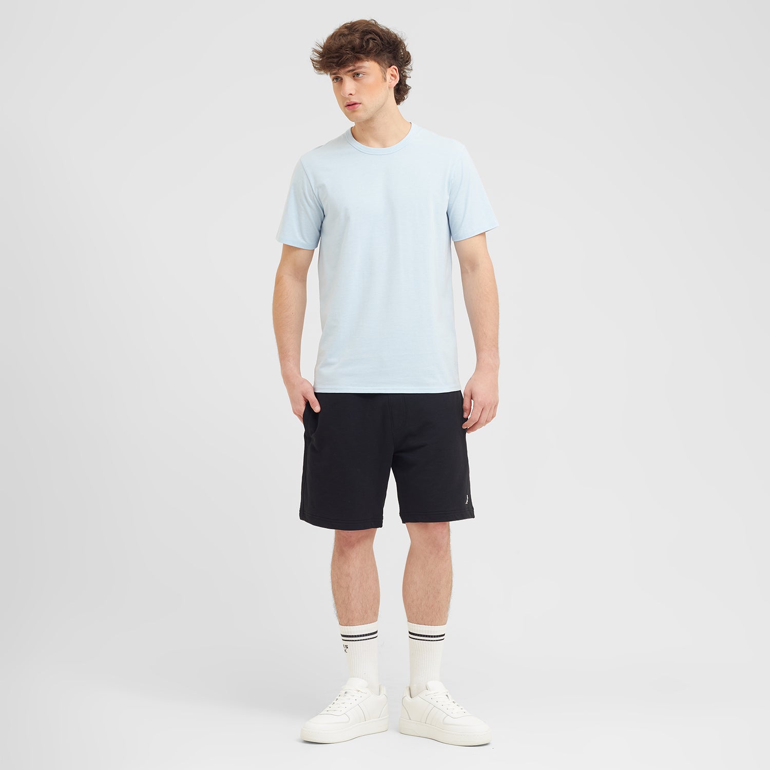 Man wearing a light blue t-shirt and black shorts on a white background
