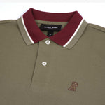 Close-up of the embroidered dog logo on the olive polo shirt: A small embroidered dog logo in maroon is visible on the left chest of the shirt.