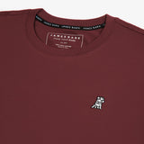 A close-up of the neckline and chest area of the maroon t-shirt, highlighting the small embroidered graphic of a dog on the left side and part of the collar tag.