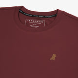 A close-up of the neckline and chest area of the maroon t-shirt, highlighting the embroidered graphic of a dog and part of the inner collar label.