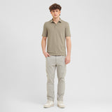 Man wearing a green polo shirt and light gray pants on a white background