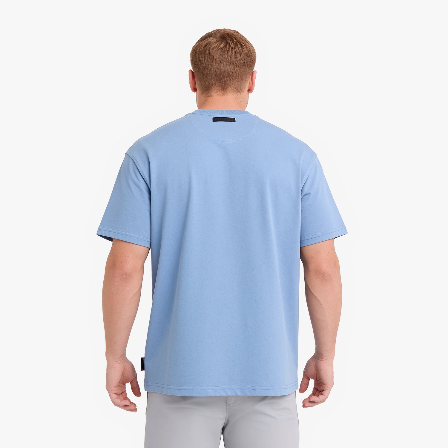 A man viewed from behind wearing a light blue short-sleeve t-shirt and light gray pants